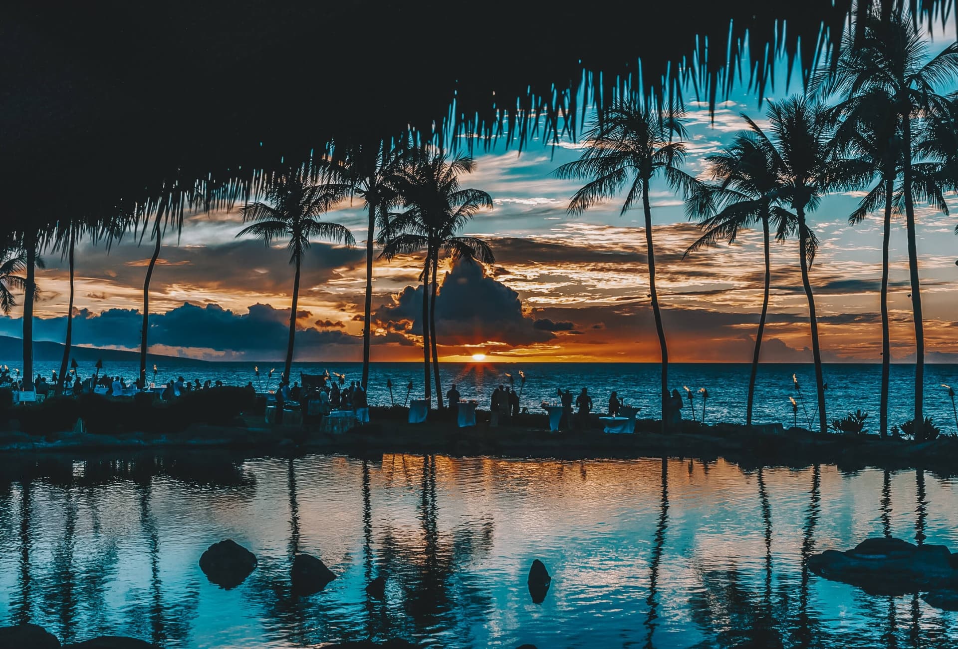 Palm trees silhouetted against an orange sunset over the ocean at Grand Wailea